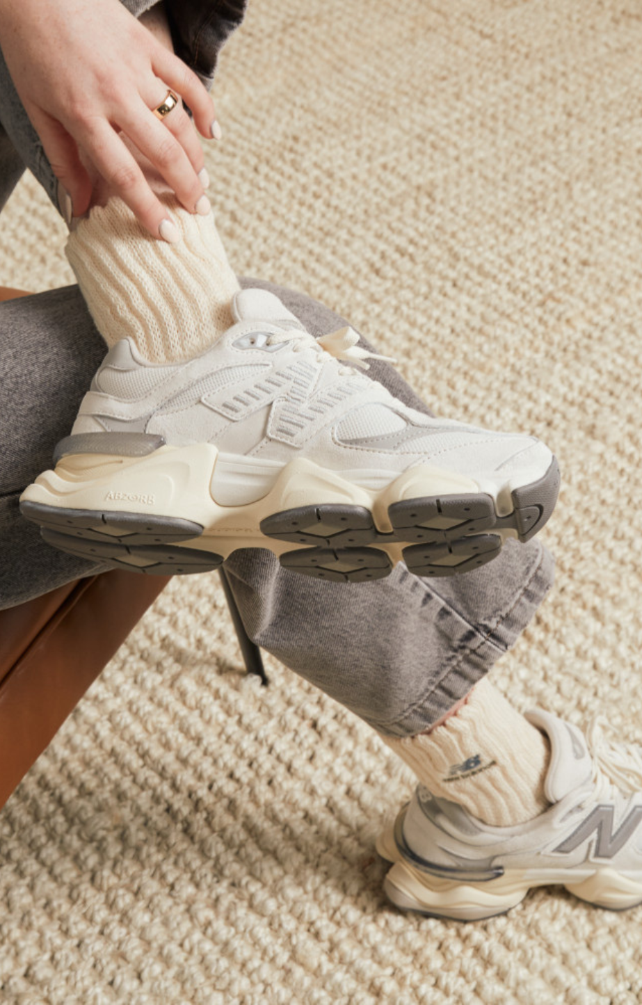 person sitting on chair cross legged wearing 9060 new balance shoes